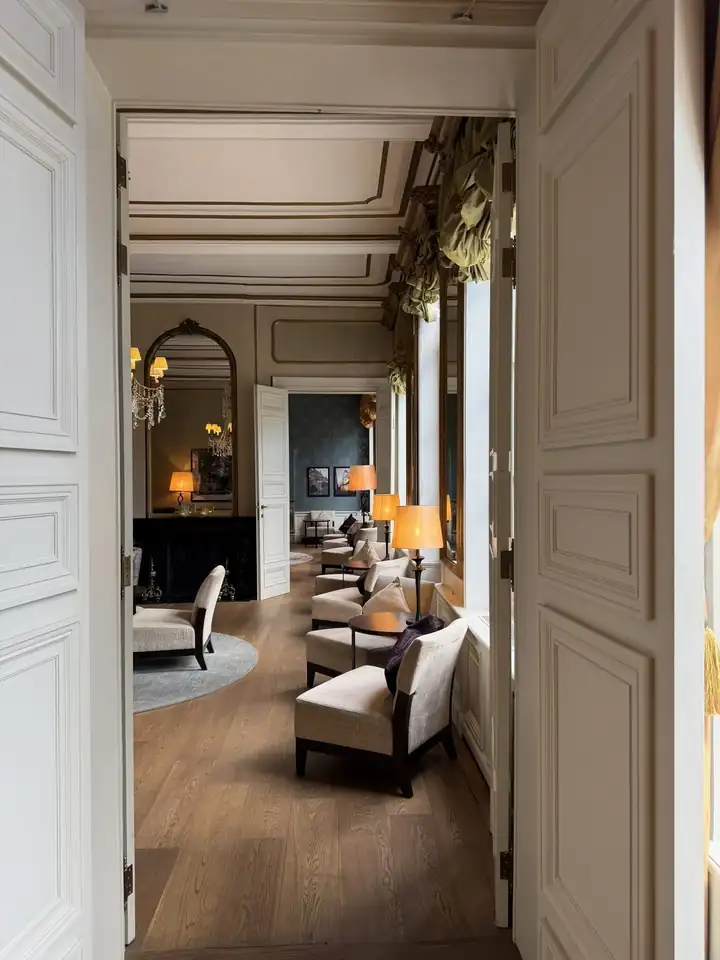 Blick durch eine Flügeltür in den Salon mit Stuckdecke, Spiegeln, Kronleuchtern und Sesseln am Fenster