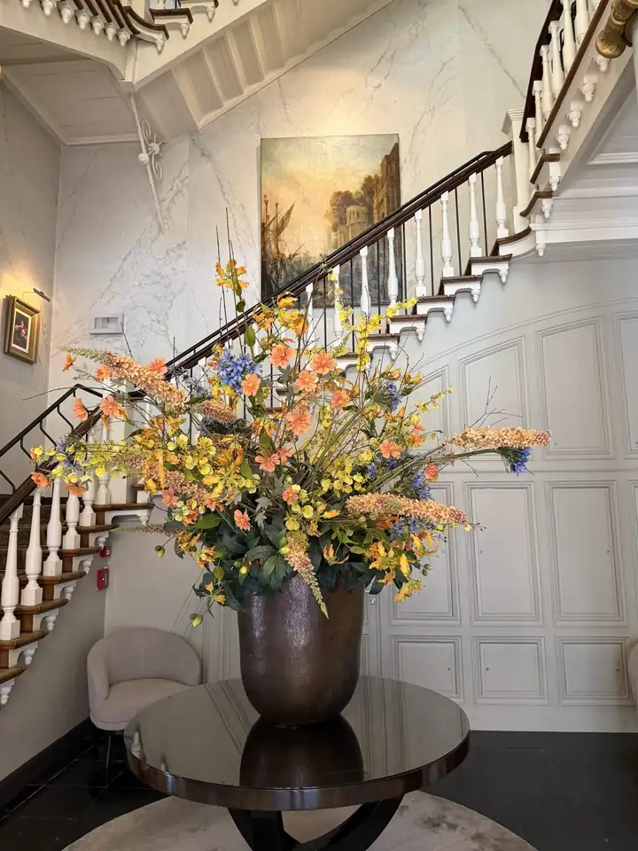 Treppenhaus im Dukes' Palace mit geschwungener Treppe, Marmorwand, Ölgemälde und großem Blumenstrauß auf einem runden Tisch