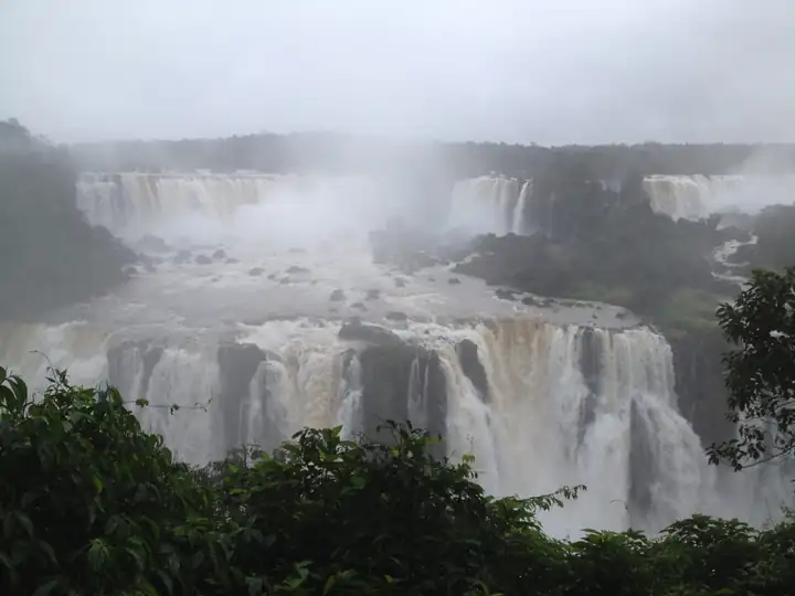 Breite Wasserfälle des Iguaçu mit braunem Wasser und Gischt über grünem Wald