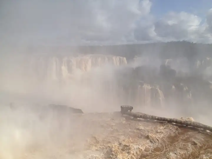 Gischt steigt aus der Schlucht der Iguaçu Fälle, darunter ein Steg über braunem Wasser
