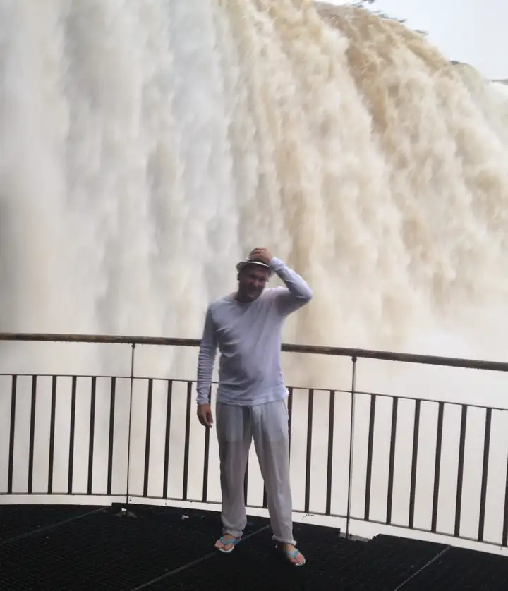 Mann im weißen Langarmshirt auf einer Aussichtsplattform direkt vor einer Wand aus herabstürzendem Wasser