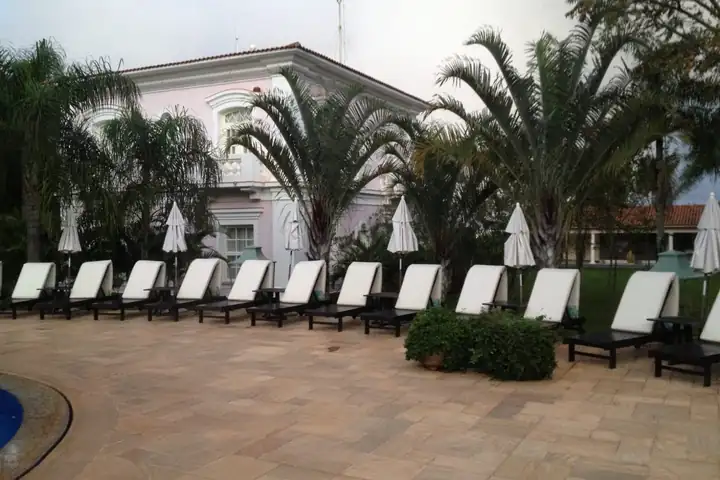 Pool des Hotel das Cataratas mit weißen Liegen und Sonnenschirmen, dahinter Palmen und das rosa und weiße Hauptgebäude