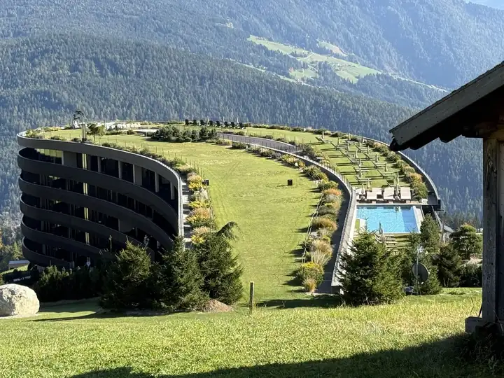 Geschwungener Hotelbau von Familiamus mit begrünter Dachwiese und Pool über dem Tal in Meransen