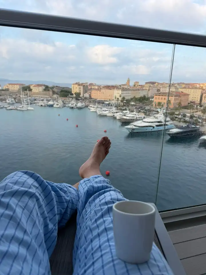 Füße auf der Balkonbrüstung, daneben eine Tasse, unten der Hafen von Ajaccio mit Yachten