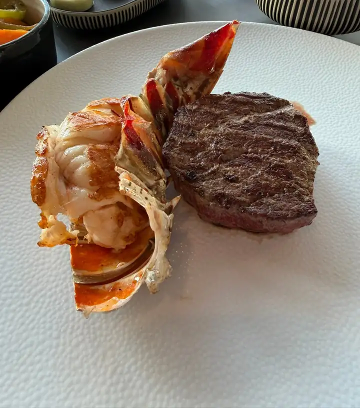 Gegrillter Hummerschwanz neben einem Steak auf einem weißen Teller