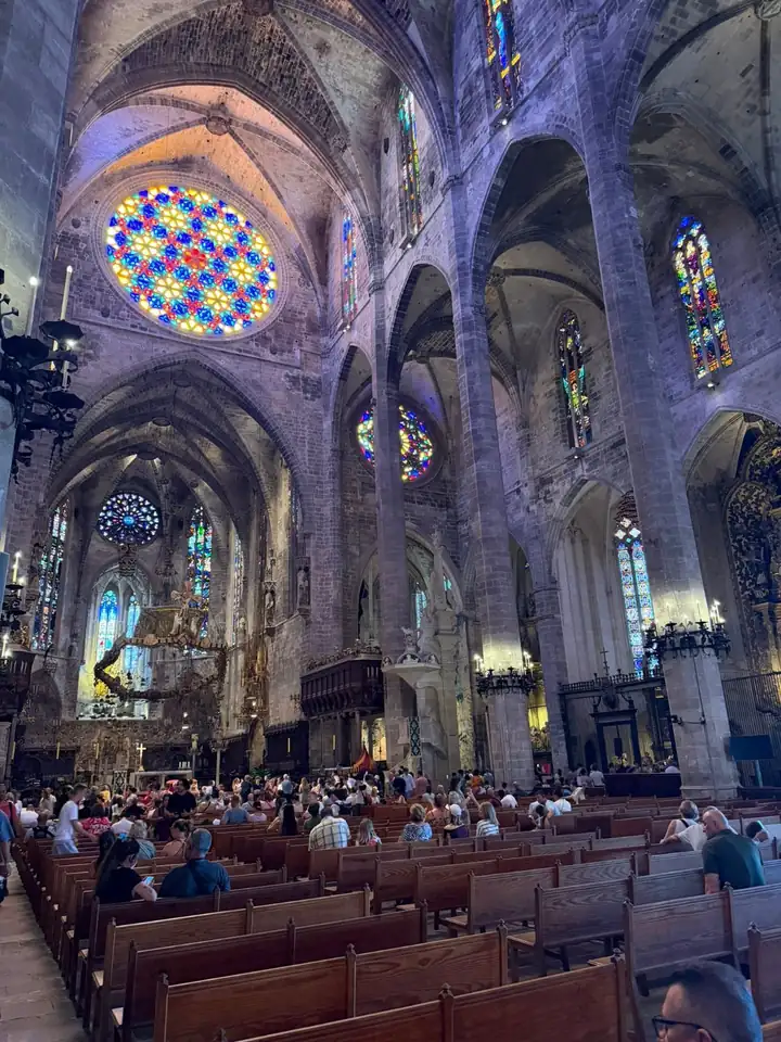 Innenraum der Kathedrale La Seu mit hohen Säulen, Kirchenbänken und der bunten Fensterrosette