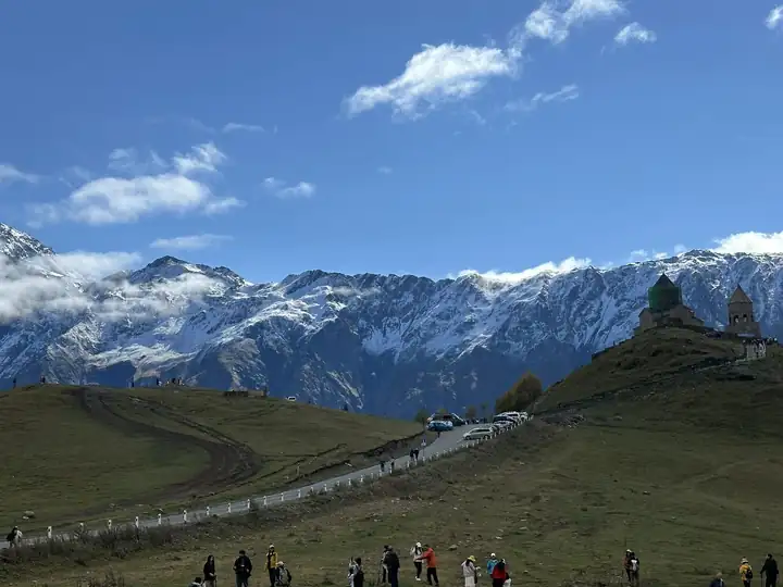 Dreifaltigkeitskirche von Gergeti auf einem grünen Hügel vor verschneiten Bergen des Großen Kaukasus