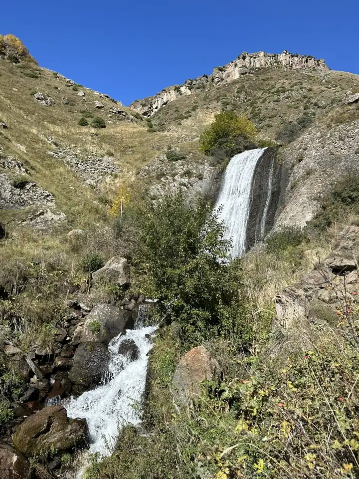 Wasserfall an einem grasbewachsenen Hang im Großen Kaukasus im Herbst