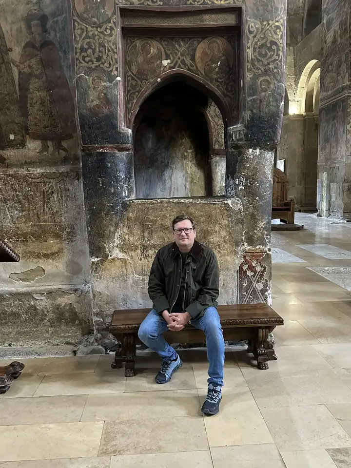 Herausgeber Lars Laschinski auf einer Holzbank vor Fresken in der Kathedrale Swetizchoweli
