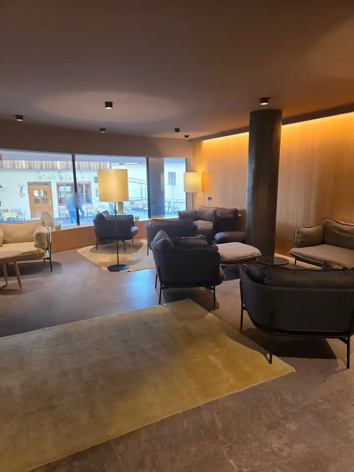Lobby des Hotel Lamm mit grauen Sesseln, Stehlampen, Holzwand mit warmem Licht und einer Säule, durch große Fenster der Blick in die Gasse