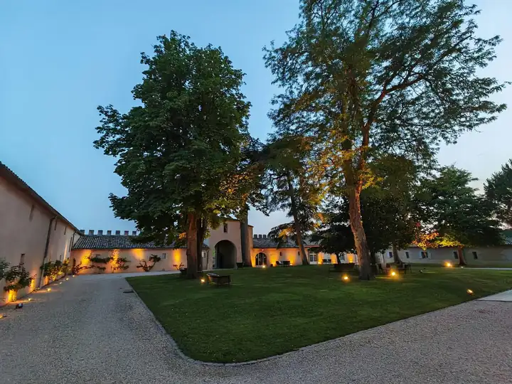 Innenhof des Château Lafaurie Peyraguey in der Dämmerung mit Rasen, zwei großen Bäumen und beleuchteter Mauer mit Zinnen