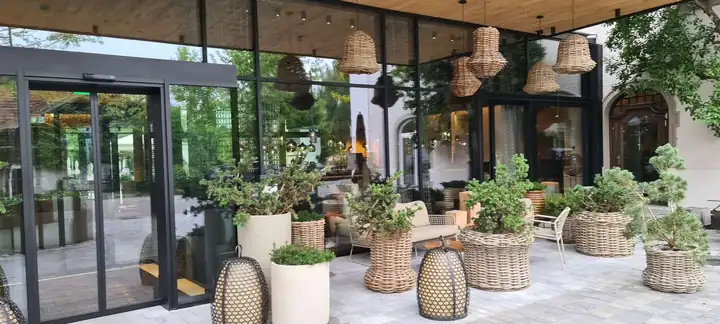 Eingang des Mühlbach mit Glastüren, Hängelampen aus Rattan und großen Körben mit Bäumchen unter einem Holzdach