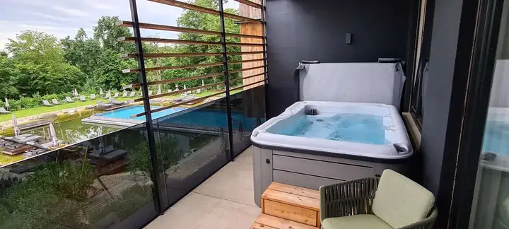 Balkon mit Whirlpool, Holzstufen und einem grünen Sessel, durch das Glasgeländer Blick auf den Pool und den Garten