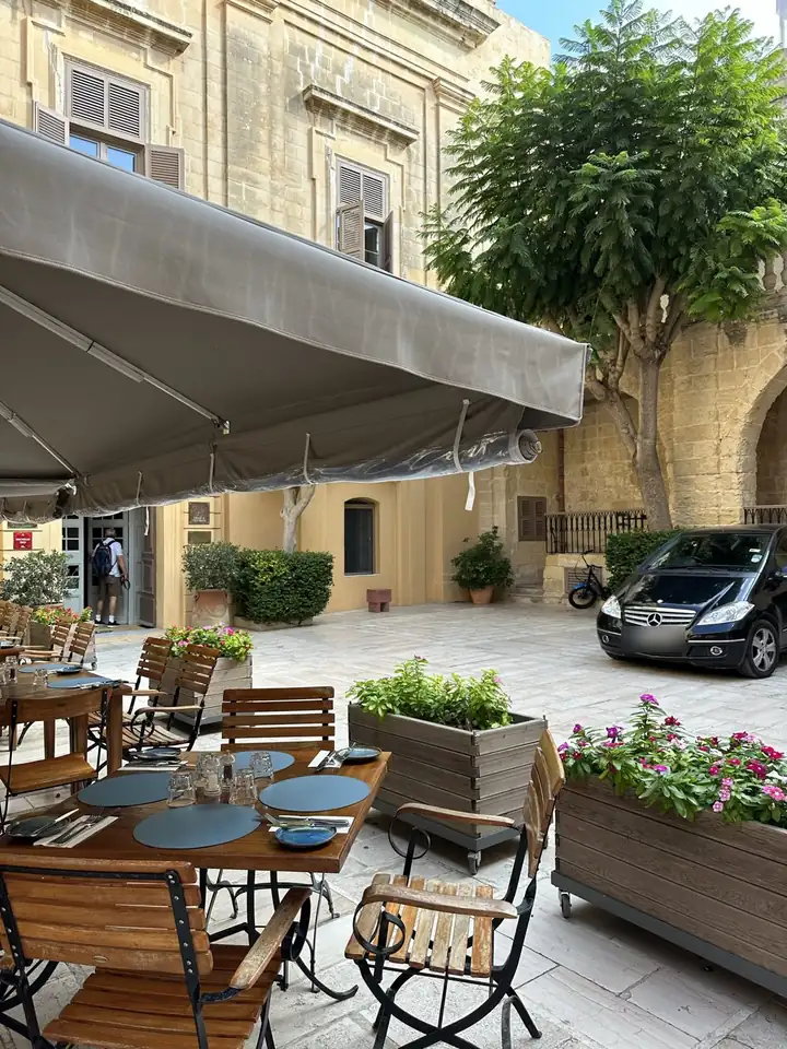 Restaurantterrasse mit Holzstühlen und Markise auf einem Platz in Mdina