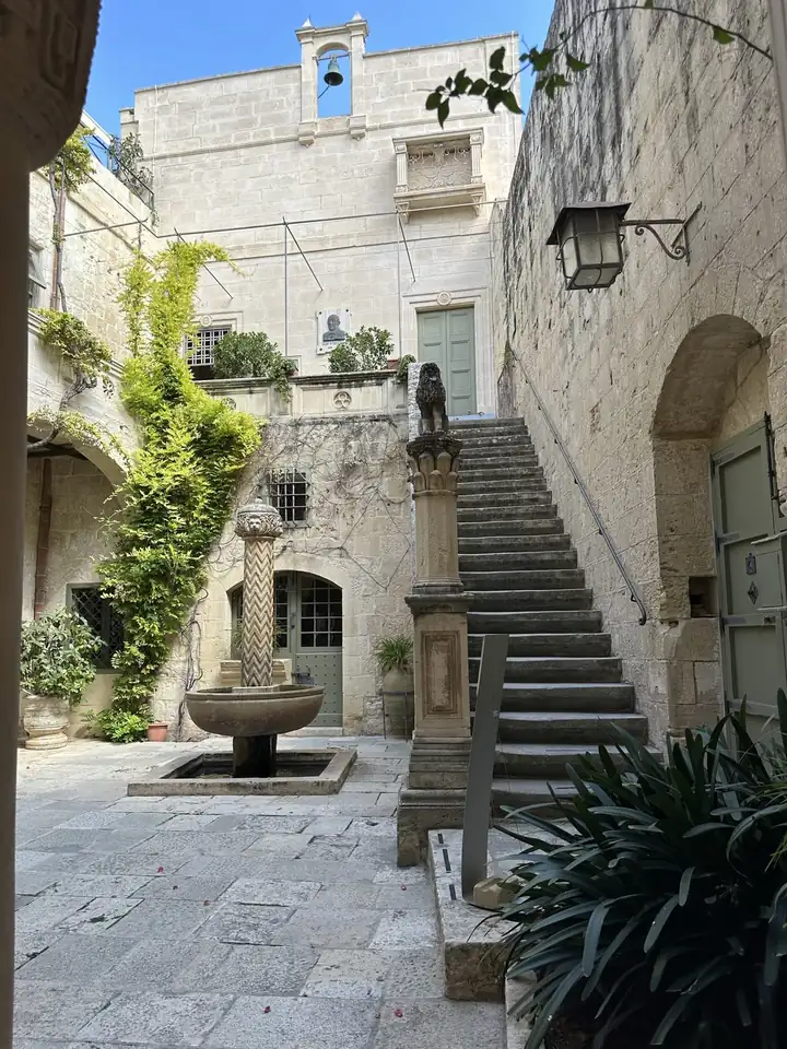 Innenhof des Palazzo Falson in Mdina mit Steintreppe, Löwensäule und Brunnen