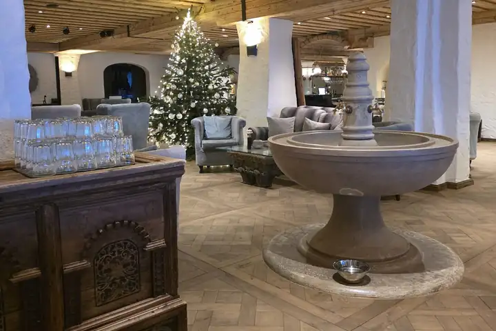 Halle des Posthotels mit Holzbalkendecke, weißen Säulen, einem Brunnen aus Stein, grauen Sesseln und einem geschmückten Christbaum