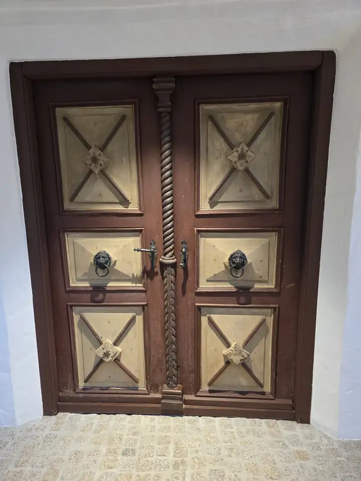 Alte zweiflügelige Holztür mit geschnitzten Feldern, Löwenköpfen als Türklopfer und gedrehter Mittelsäule in einer weißen Wand