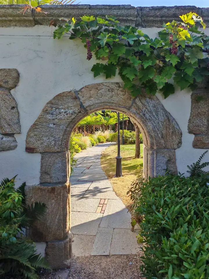 Rundbogen aus Stein in einer weißen Mauer mit Weinlaub, dahinter ein Weg durch den Garten
