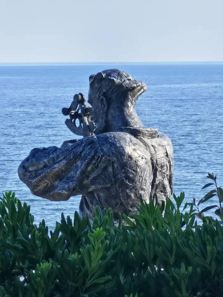 Statue eines Seefahrers mit Sextant, der über Büsche hinweg auf den Atlantik blickt
