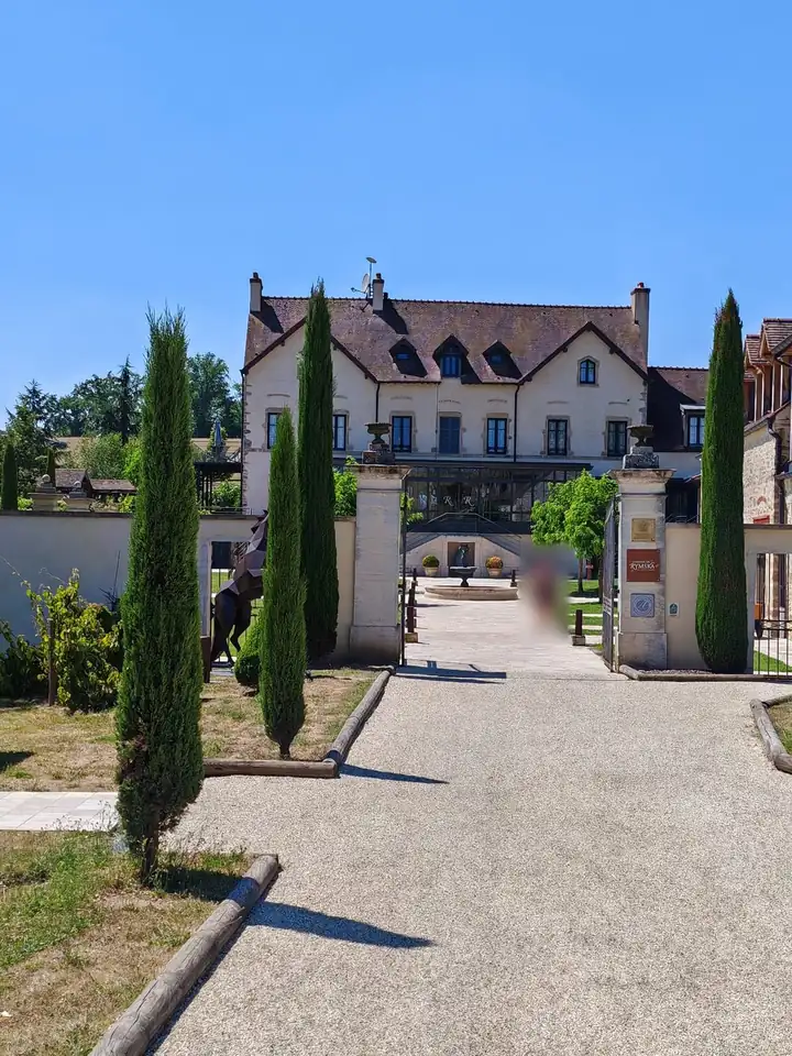 Weg zwischen Zypressen zum Tor des Domaine de Rymska, dahinter das Herrenhaus mit Brunnen im Hof