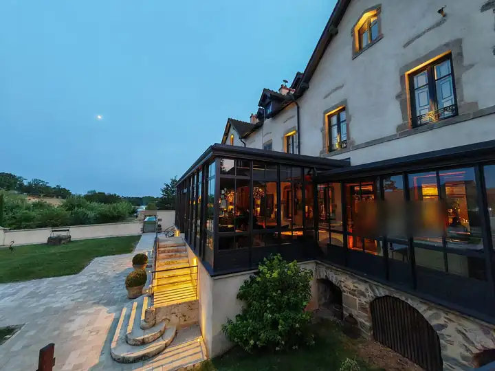 Wintergarten aus schwarzem Stahl und Glas am Herrenhaus, abends beleuchtet, daneben eine Treppe aus Stein