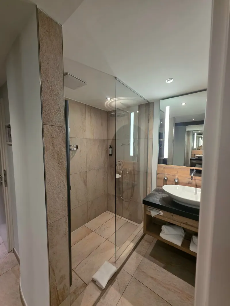 Bad mit bodengleicher Dusche hinter Glas, Fliesen in Holzoptik und Waschtisch mit Aufsatzbecken