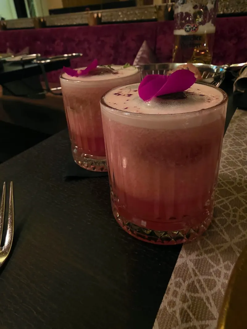 Zwei rosa Cocktails mit lila Blüten auf einem dunklen Tresen in der Bar