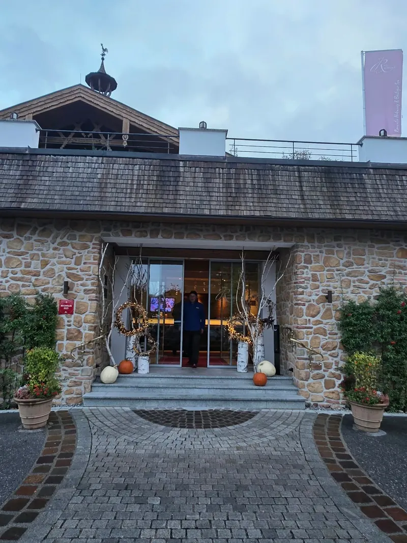 Eingang des Hotels mit Natursteinmauern, Glastür, Kürbissen und Topfpflanzen, davor ein gepflasterter Hof