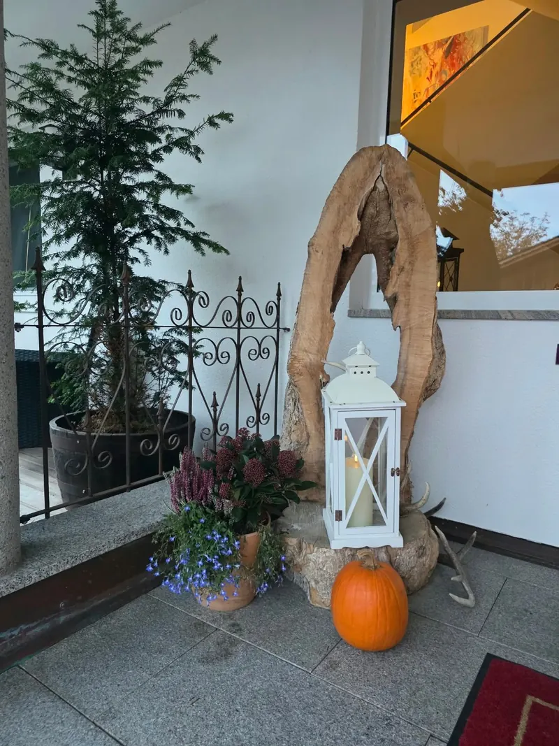 Eingang mit Laterne, Kürbis, Heidekraut und einer Skulptur aus Wurzelholz neben einem schmiedeeisernen Gitter