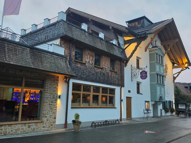 Das Rübezahl von der Straße aus: Natursteinsockel, Holzschindeln, weißer Turm mit Wirtshausschild, links die beleuchtete Bar hinter großen Fenstern