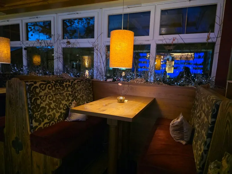 Holzgetäfelte Nische mit gemusterten Polstern und einem Tisch unter einer orangefarbenen Hängelampe, draußen blaues Licht