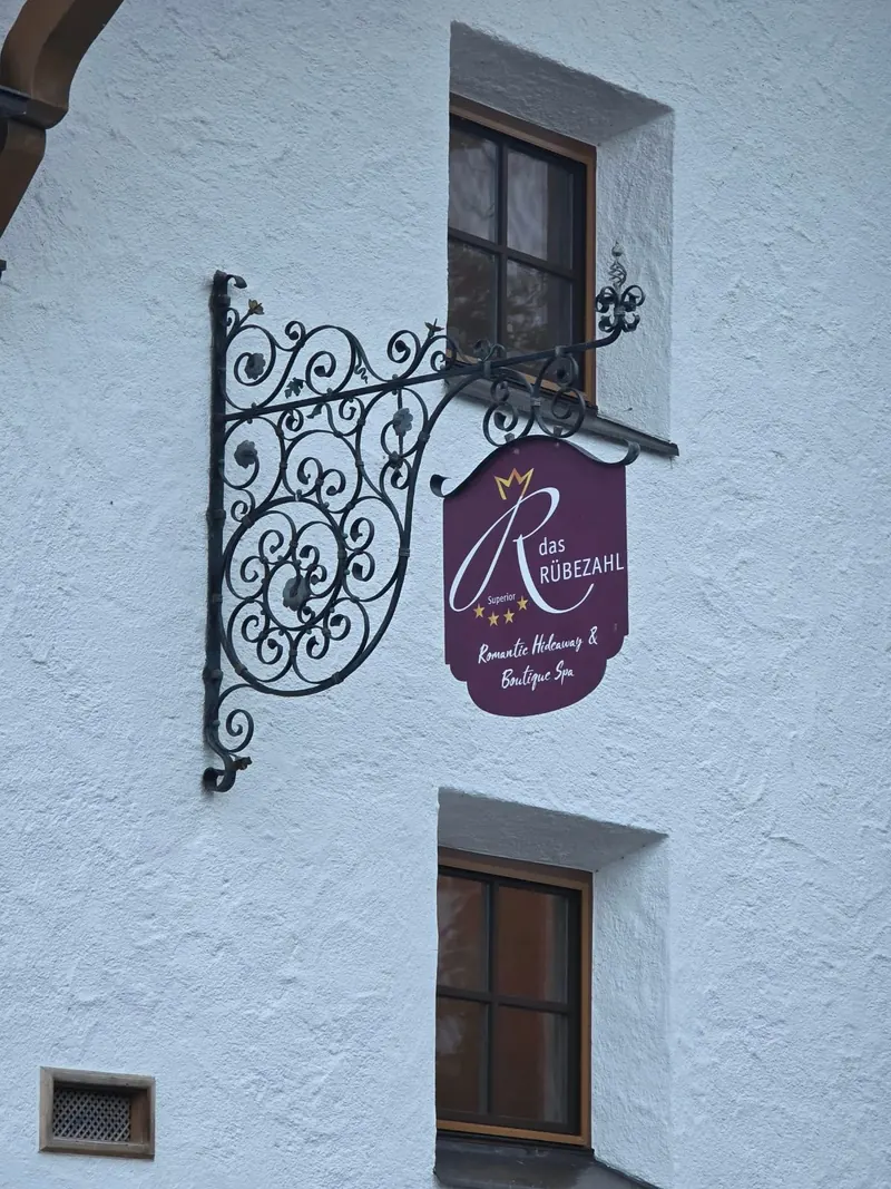 Schmiedeeisernes Wirtshausschild in Weinrot an der weißen Fassade mit dem Schriftzug das Rübezahl, Superior, Romantic Hideaway und Boutique Spa