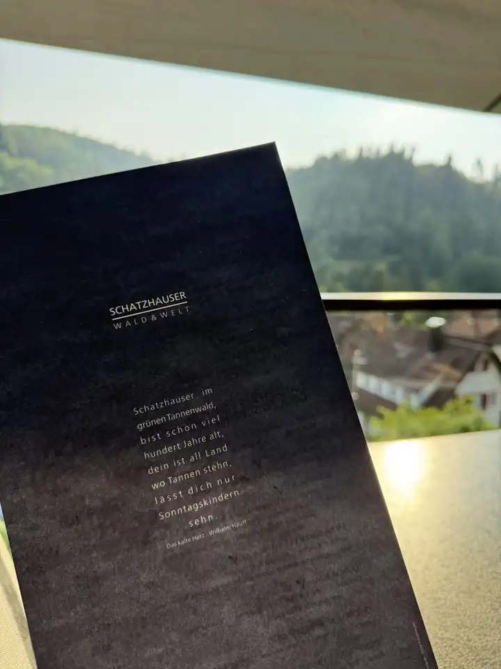 Dunkle Speisekarte des Schatzhauser mit einem Vers aus Wilhelm Hauffs Das kalte Herz, im Hintergrund bewaldete Hänge