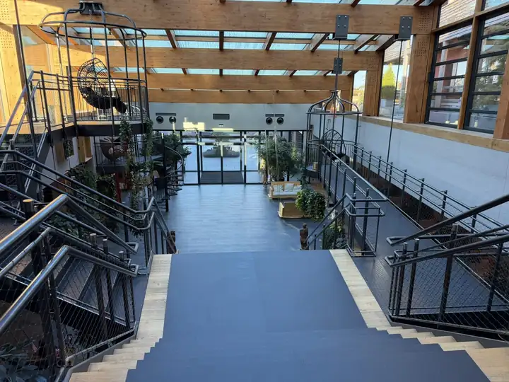 Atrium unter dem Glasdach mit Treppen aus Metall, Pflanzen und Sesseln in Vogelkäfigen
