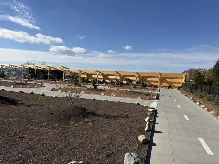 Neue Fahrbahn für Tretautos mit weißer Mittellinie, frisch gepflanzten Bäumen und einem Holzdach im Bau