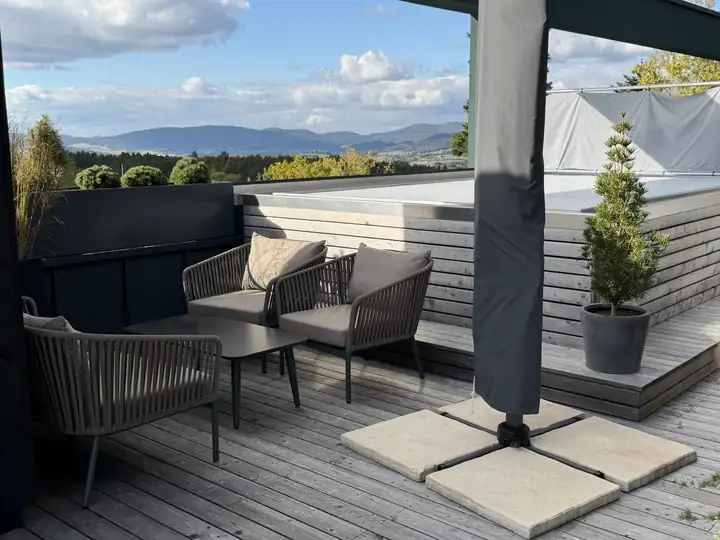 Dachterrasse der Suite mit geflochtenen Sesseln, Sonnenschirm und Blick über die Hügel des Bayerischen Waldes