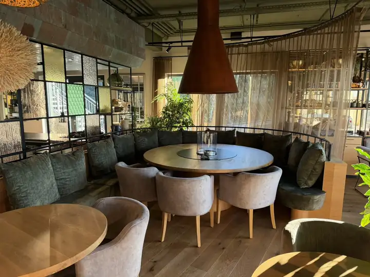 Runder Tisch mit hellen Sesseln unter einem hängenden Kamin aus Kupfer, dahinter eine geschwungene grüne Sitzbank im Restaurant OHM