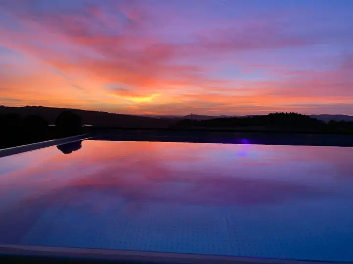 Abendrot über den Hügeln des Bayerischen Waldes, das sich im privaten Pool der Penthouse Pool Suite spiegelt