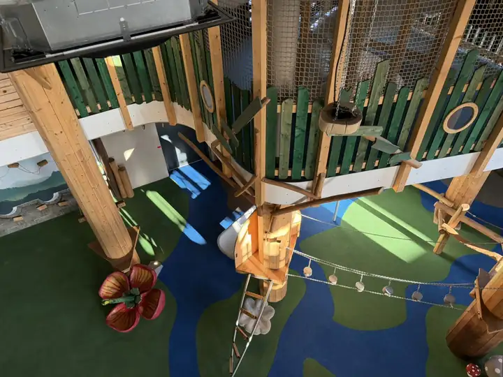Kletterlandschaft aus Holz mit Netzen, Hängebrücke und Pilzen auf blauem und grünem Boden in der Spielkiste