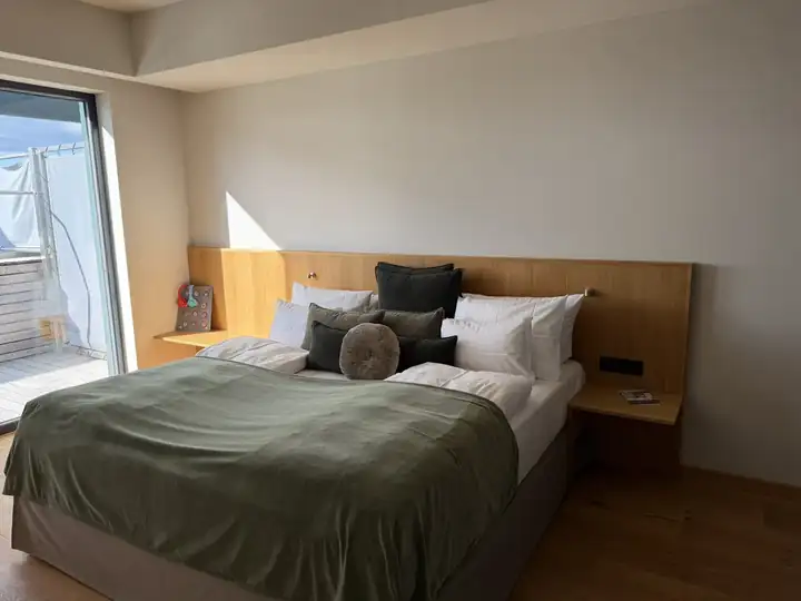 Elternschlafzimmer im Penthouse mit grüner Tagesdecke, Kopfteil aus Holz und Tür zur Dachterrasse