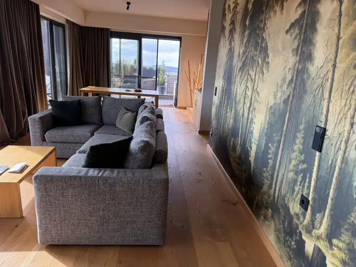 Wohnraum des Penthouse 501 mit grauem Ecksofa, Waldtapete und Fenster zur Terrasse