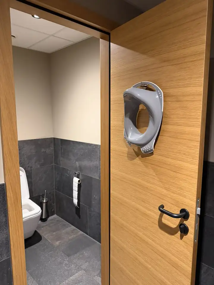 Toilettensitz für Kinder an einem Haken innen an der Tür eines WC mit grauen Fliesen