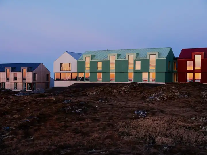 Häuser des Ytri Island Retreat in Grün, Weiß und Rot auf der Heide von Husøy im Abendlicht