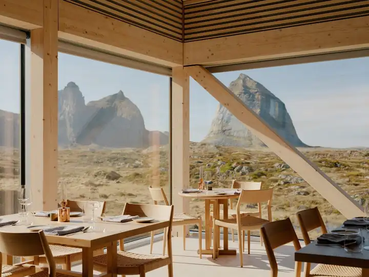 Restaurant Alma mit Holztischen und Stühlen mit Papiergeflecht vor Panoramafenstern, draußen die Berge von Sanna