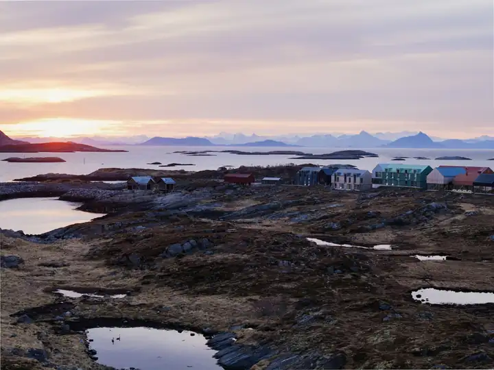 Fels und Wasserlachen auf Husøy, dahinter die farbigen Häuser des Hotels und Inseln im Abendlicht