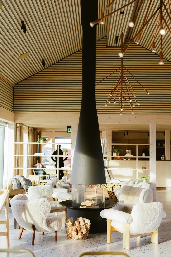 Lounge mit hängendem schwarzem Kamin, Sesseln mit Fellbezug, Regalen aus hellem Holz und einer Leuchte aus Kupfer