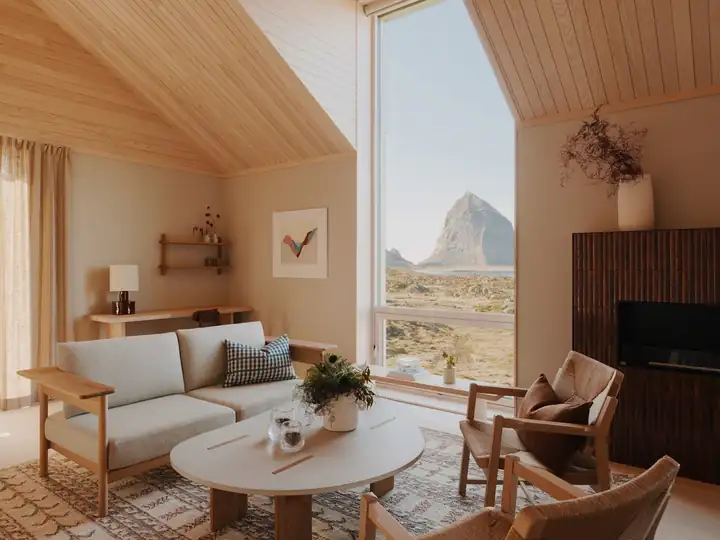 Wohnbereich einer Suite mit hellem Sofa, rundem Tisch, Holzsesseln und großem Fenster mit Blick auf den Trænstaven