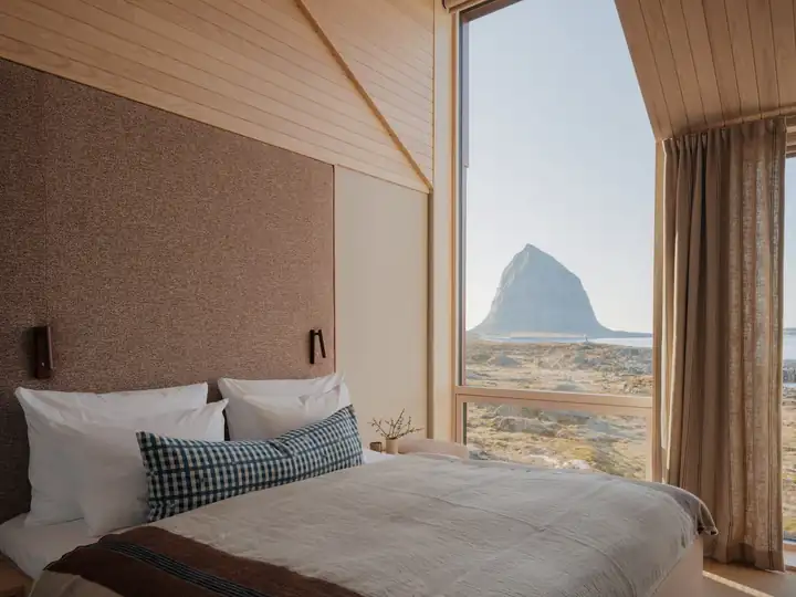 Schlafzimmer mit Holzdecke, Bett mit Kissen in Blau und Weiß und Fenster mit Blick auf den Trænstaven